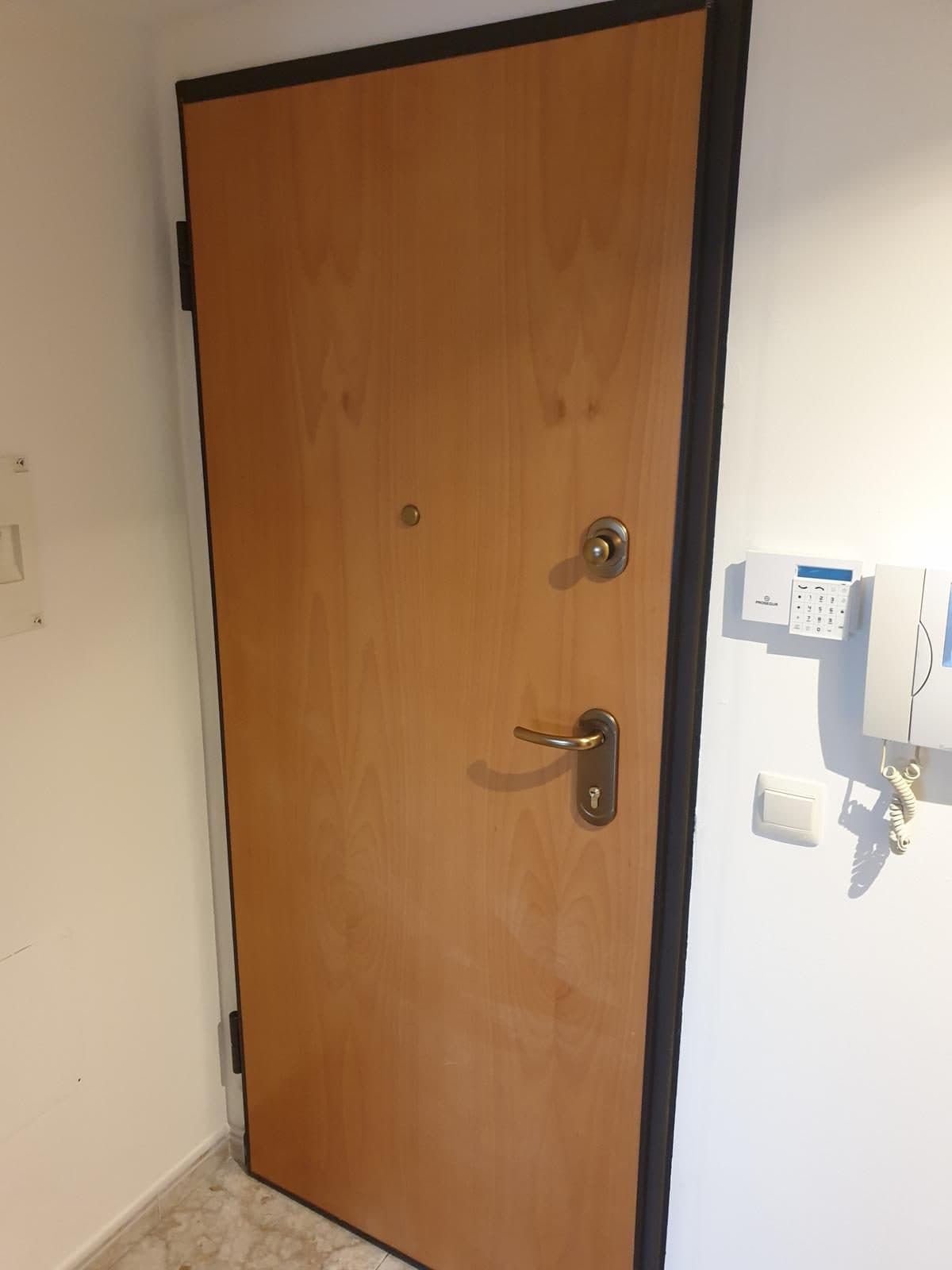 Puerta blindada de madera clara con cerradura de seguridad, instalada en un recibidor